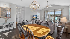 A spacious living room with a wooden dining table, comfortable seating, a chandelier, and a view of the outdoors. - Ironwood | Pool & Tennis Near the Beach (North Myrtle Beach)