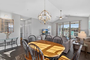A spacious living room with a wooden dining table, comfortable seating, a chandelier, and a view of the outdoors. - Ironwood | Pool & Tennis Near the Beach (North Myrtle Beach)