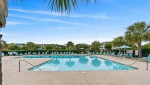 A rectangular pool with a clear blue water surface, surrounded by a sandy area with green lounge chairs and umbrellas. - Ironwood | Pool & Tennis Near the Beach (North Myrtle Beach)