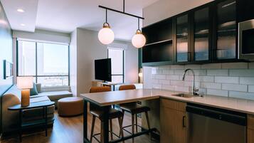 A modern kitchen with a central island, bar stools, and a dining area with a sofa and table.