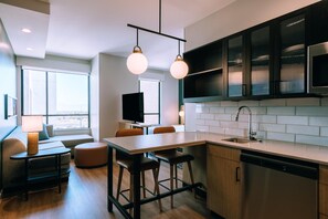 A modern kitchen with a central island, bar stools, and a dining area with a sofa and table. - Hyatt House Ontario Airport (Ontario)