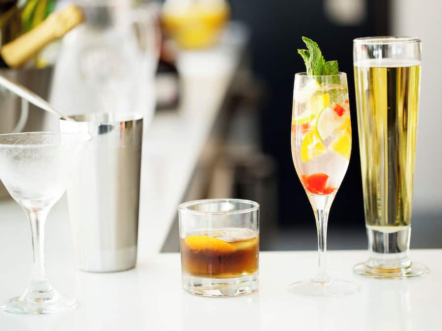 Três tipos diferentes de copos sobre uma mesa, incluindo um copo de martini, um copo baixo e um copo longo de champanhe.