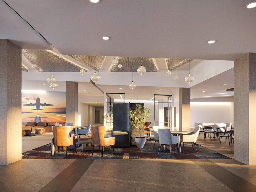 Een moderne hotel lobby met een zithoek, een grote plant en een muurschildering van een vliegtuig.