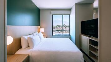 Habitación de hotel con cama, televisor, ventana con vistas y lámpara.
