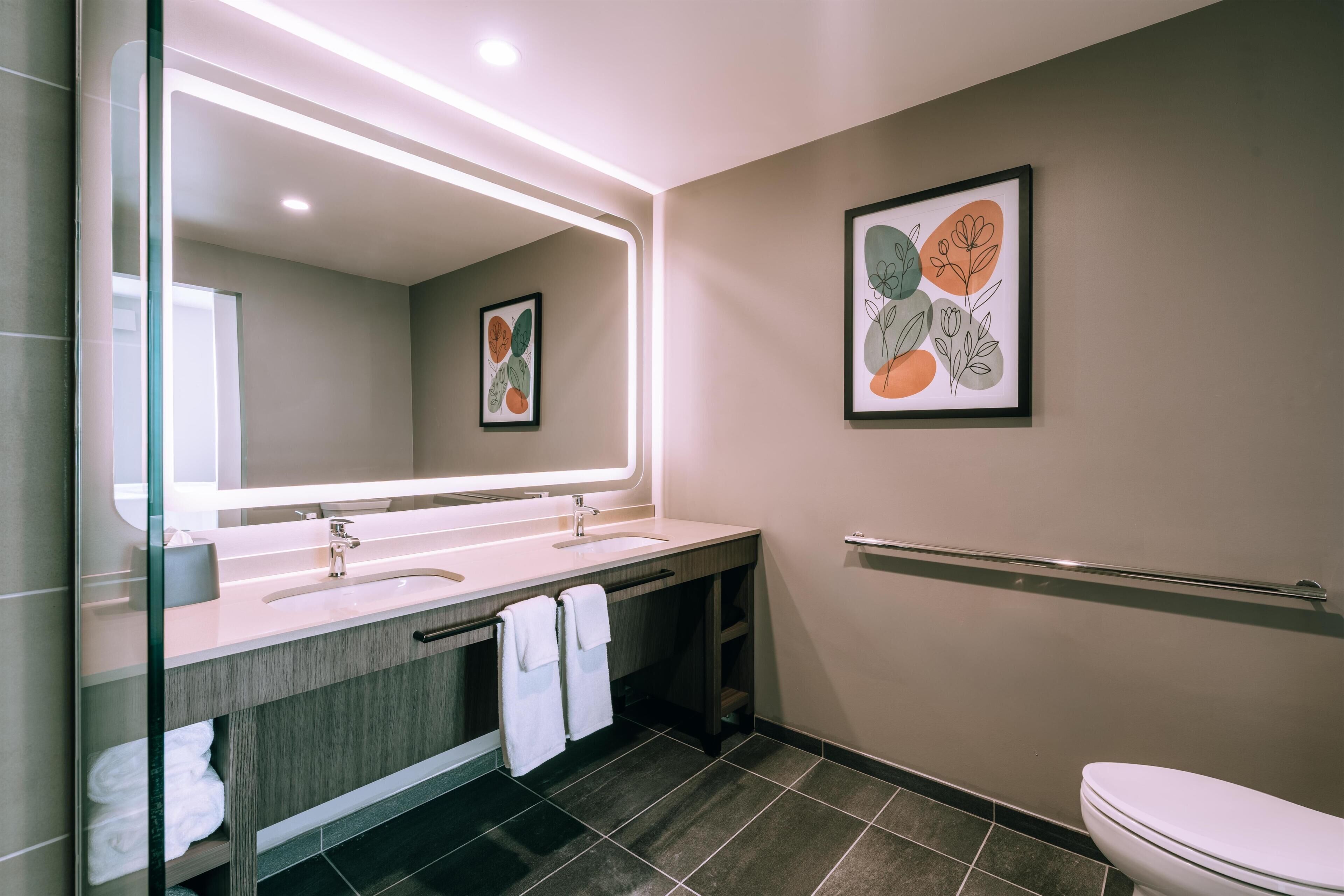Un baño moderno con un espejo grande, dos lavamanos, un inodoro y un perchero para toallas.