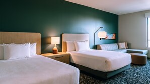 A hotel room with two beds, a desk, a lamp, a sofa, and a painting on the wall. - Hyatt House Ontario Airport (Ontario)