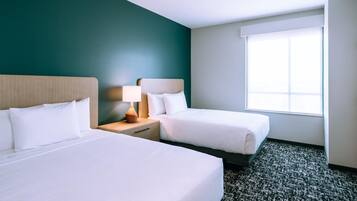A hotel room with two beds, a nightstand with a lamp, and a large window providing natural light.