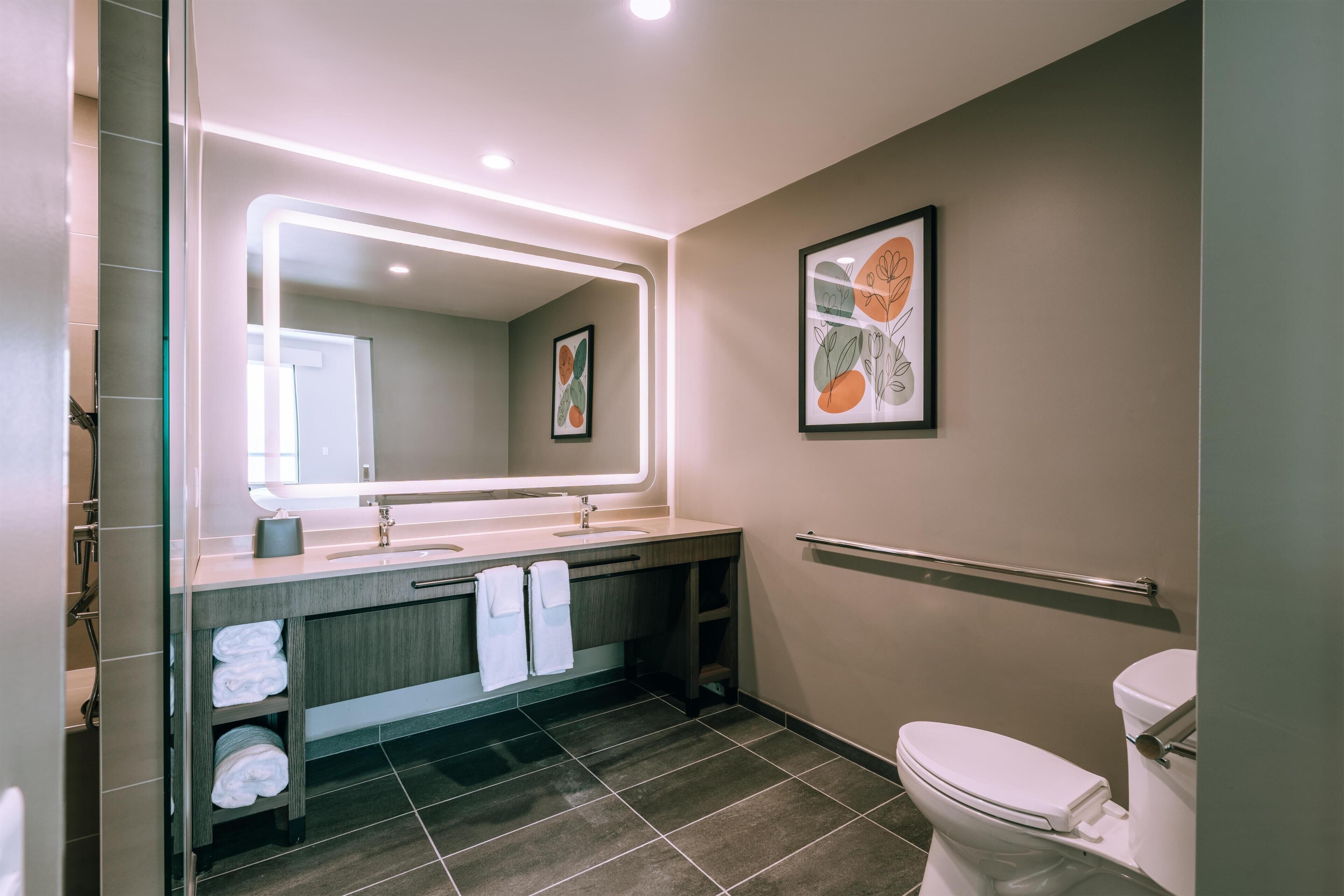 Un baño moderno con un espejo grande, lavamanos dobles, un inodoro y un perchero para toallas.