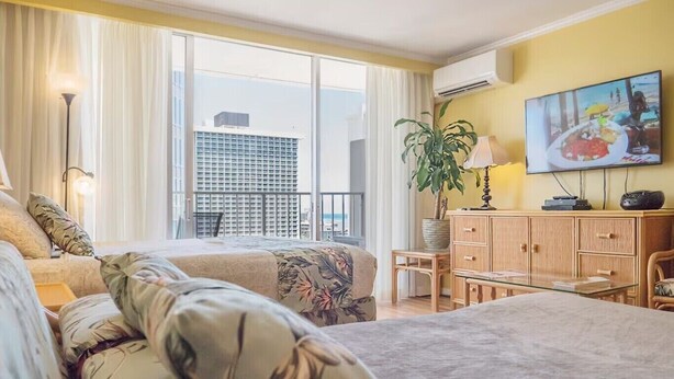 Habitación de hotel con una cama grande, un escritorio, una silla, una planta en maceta y un televisor en la pared.