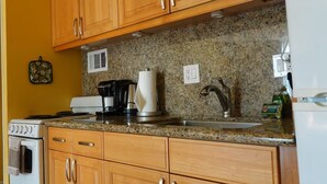 Una cocina con armarios de madera, encimera de granito, estufa, cafetera y lavabo.