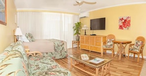 A hotel room with a bed, a sofa, a glass coffee table, a wooden cabinet, a TV, and a painting on the wall. - Premium Bright City-View Retreat - Any Premium Rm (Honolulu)