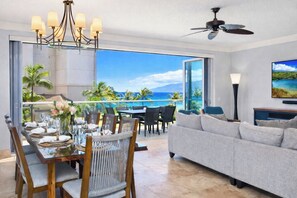 Ein Essbereich mit Meerblick, ein Wohnzimmer mit Sofa und Fernseher sowie ein Deckenventilator.