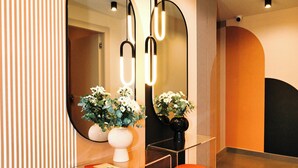 Ein moderner Empfangsbereich mit einem großen Spiegel, zwei roten Poufs und einer Blumenvase.