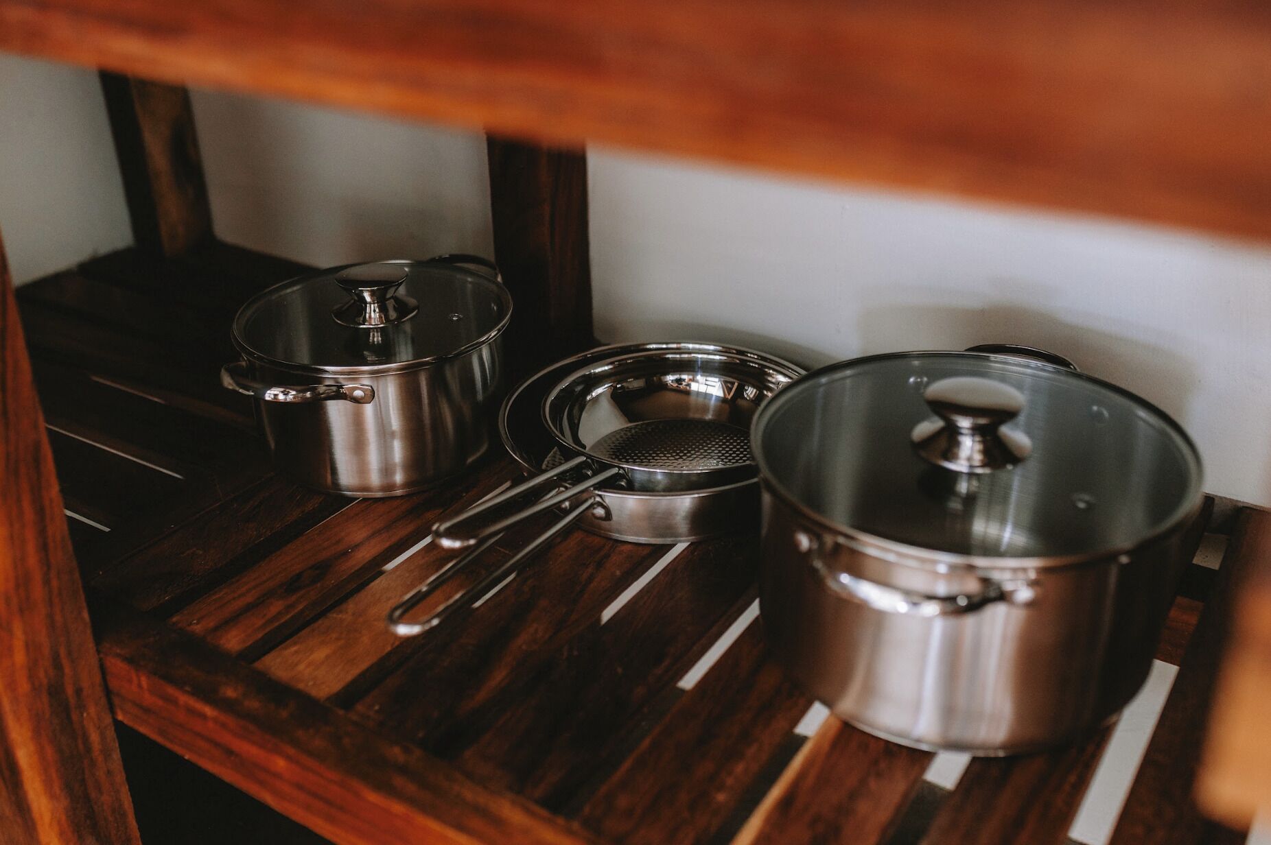 A wooden shelf with three stainless steel pots and a ladle.