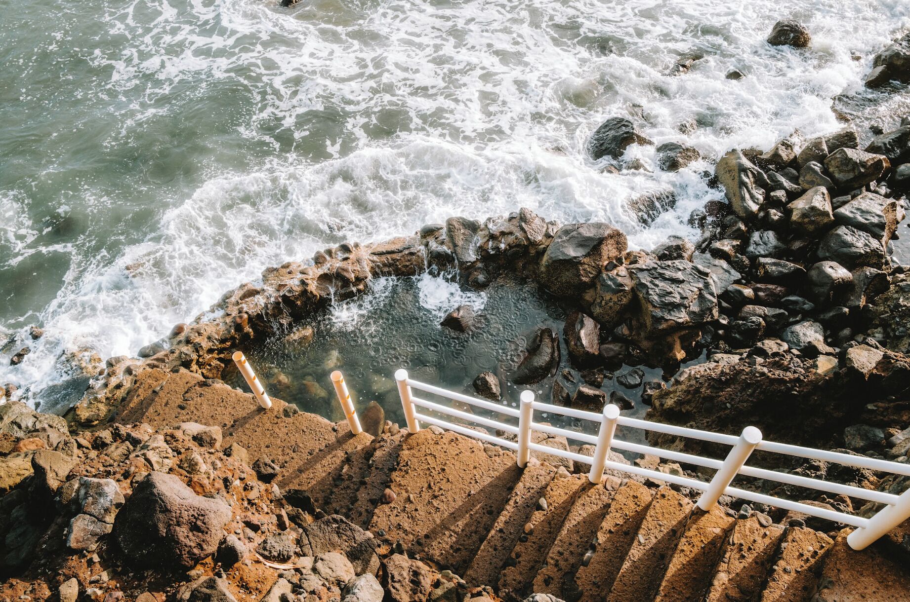 A rocky staircase leading to a beach with waves crashing nearby.