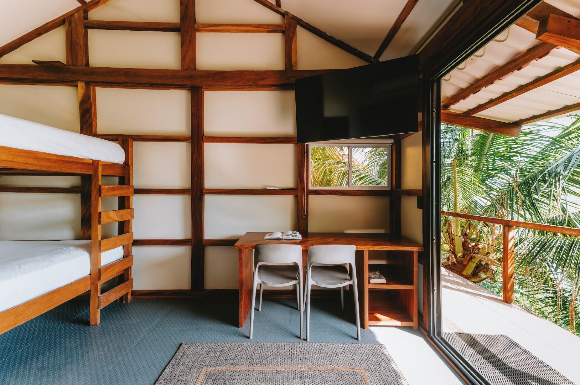 Una habitación con una litera, un escritorio con dos sillas y una ventana que da a palmeras.