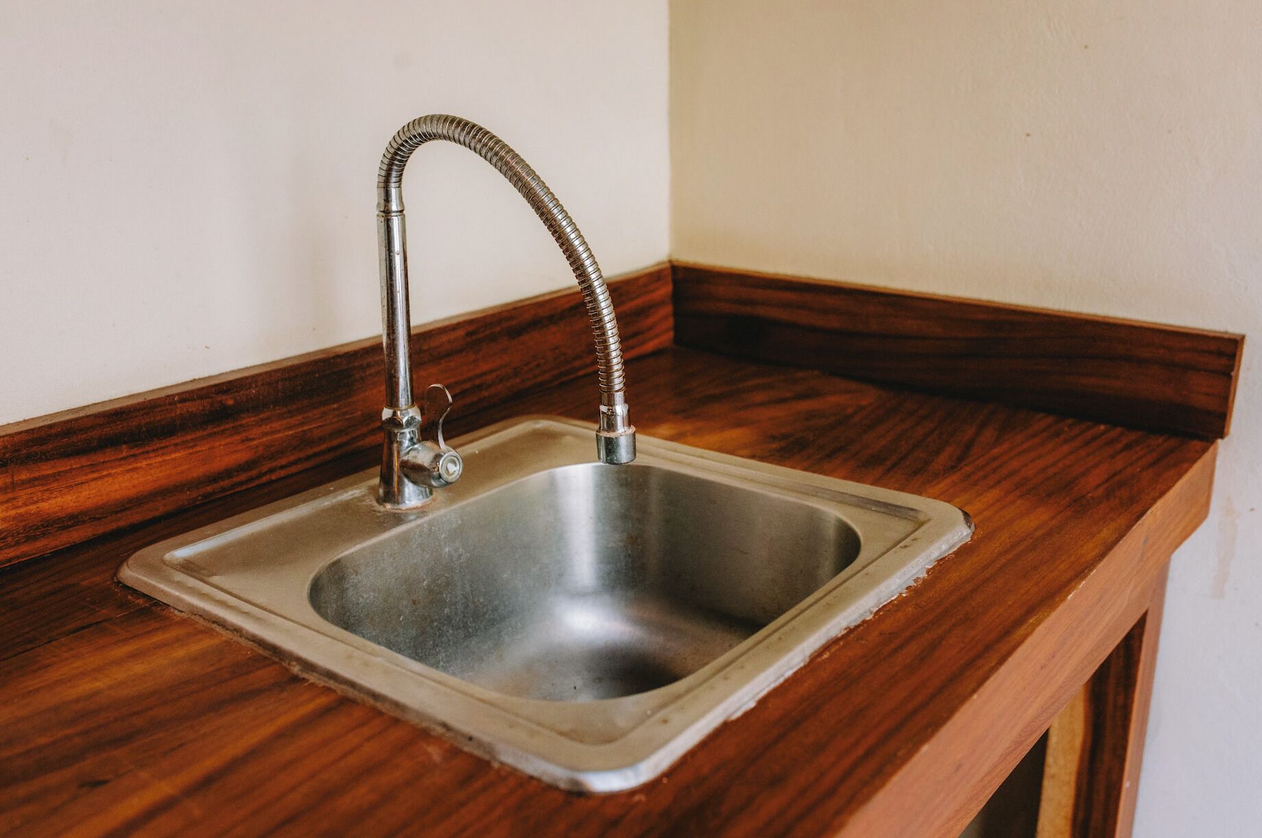 A stainless steel kitchen sink with a flexible hose faucet, set in a wooden countertop with a wooden baseboard.