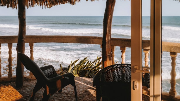 A beachside view from a covered area with a railing, two chairs, and a potted plant. - Punta Mango Villas (Jucuaran)