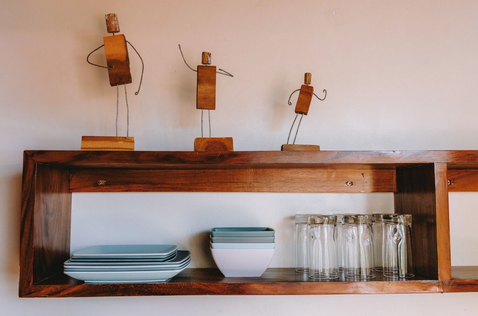 A wooden shelf with decorative metal figures, stacked plates, and clear glassware.