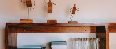 A wooden shelf with decorative metal figures, stacked plates, and clear glassware.