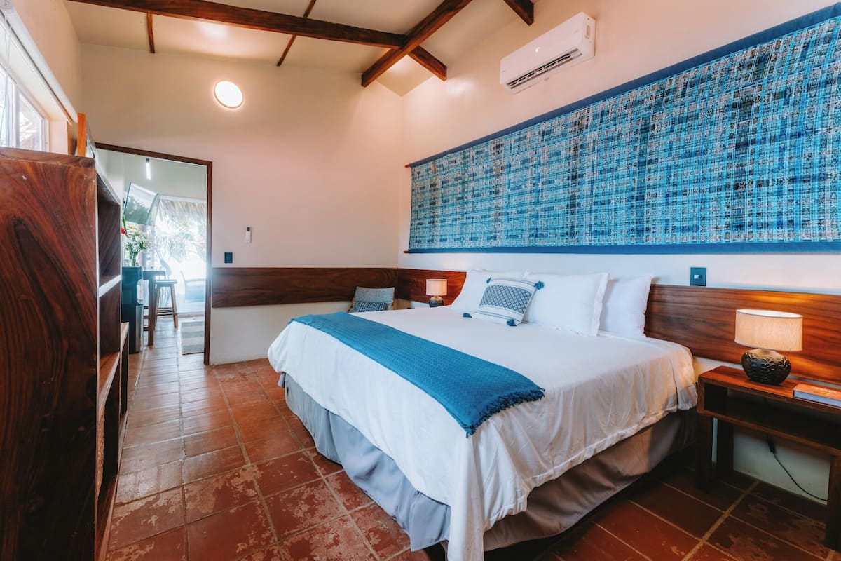 A hotel room with a large bed, wooden headboard, a blue patterned tapestry, and a tiled floor.