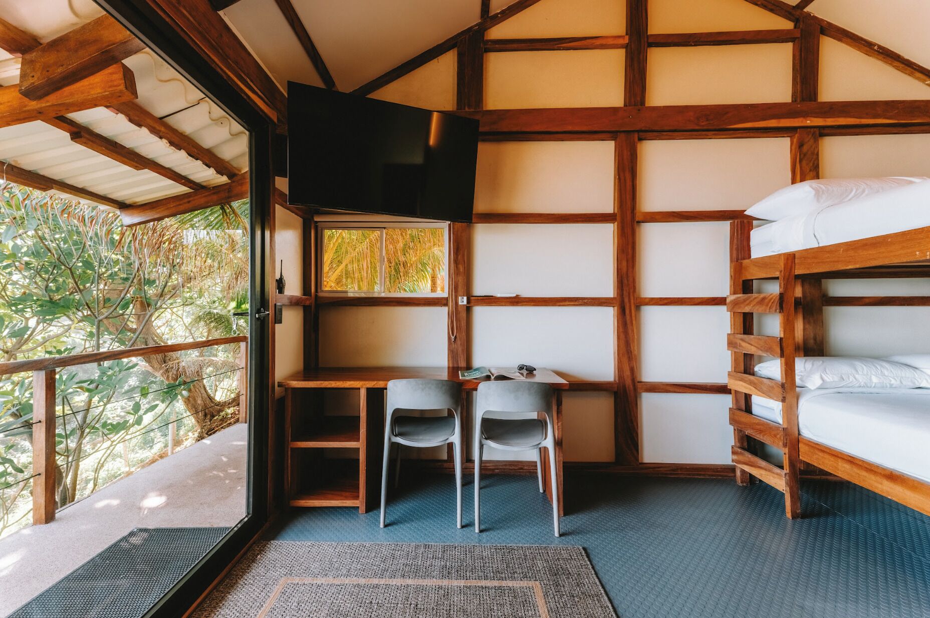 A cozy cabin with a wooden interior, a bunk bed, a desk with two chairs, and a window overlooking greenery.