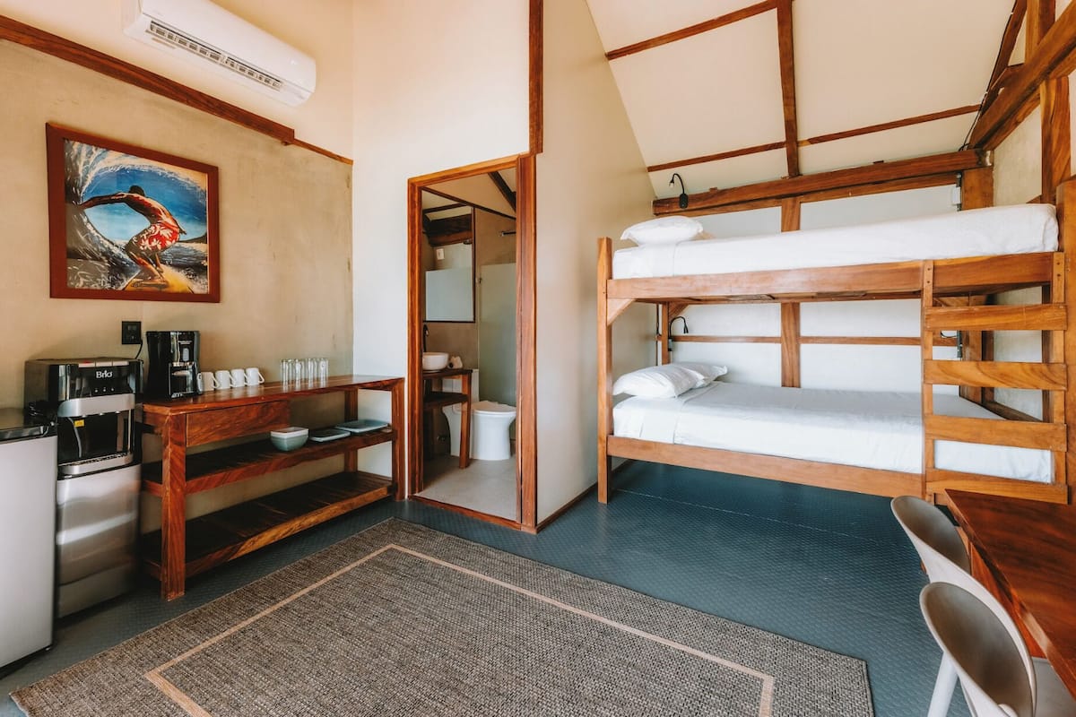 A compact room with a bunk bed, a coffee machine, a desk, and a painting on the wall.
