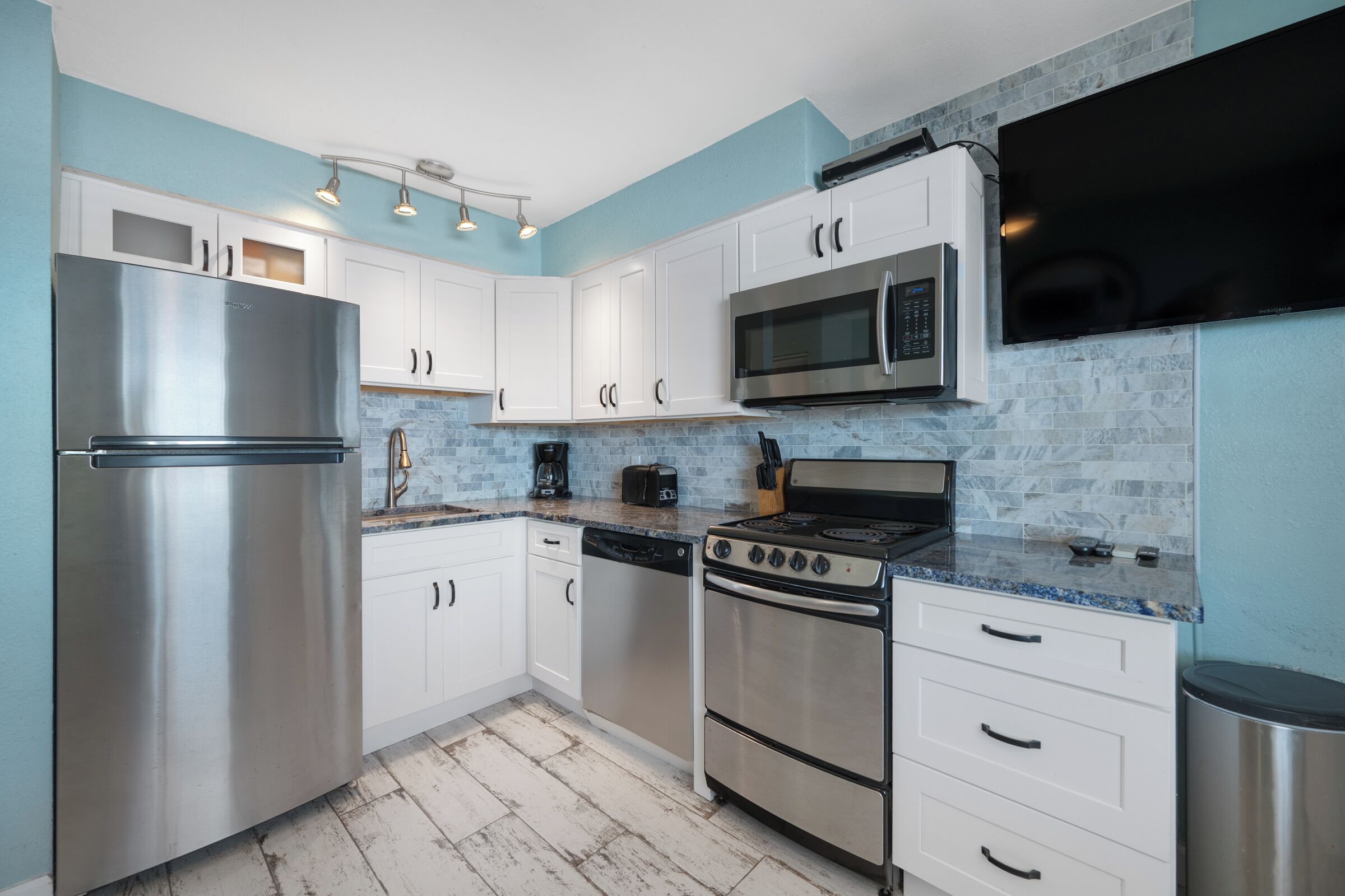 Una cocina moderna con electrodomésticos de acero inoxidable, armarios blancos y una pared de acento azul.