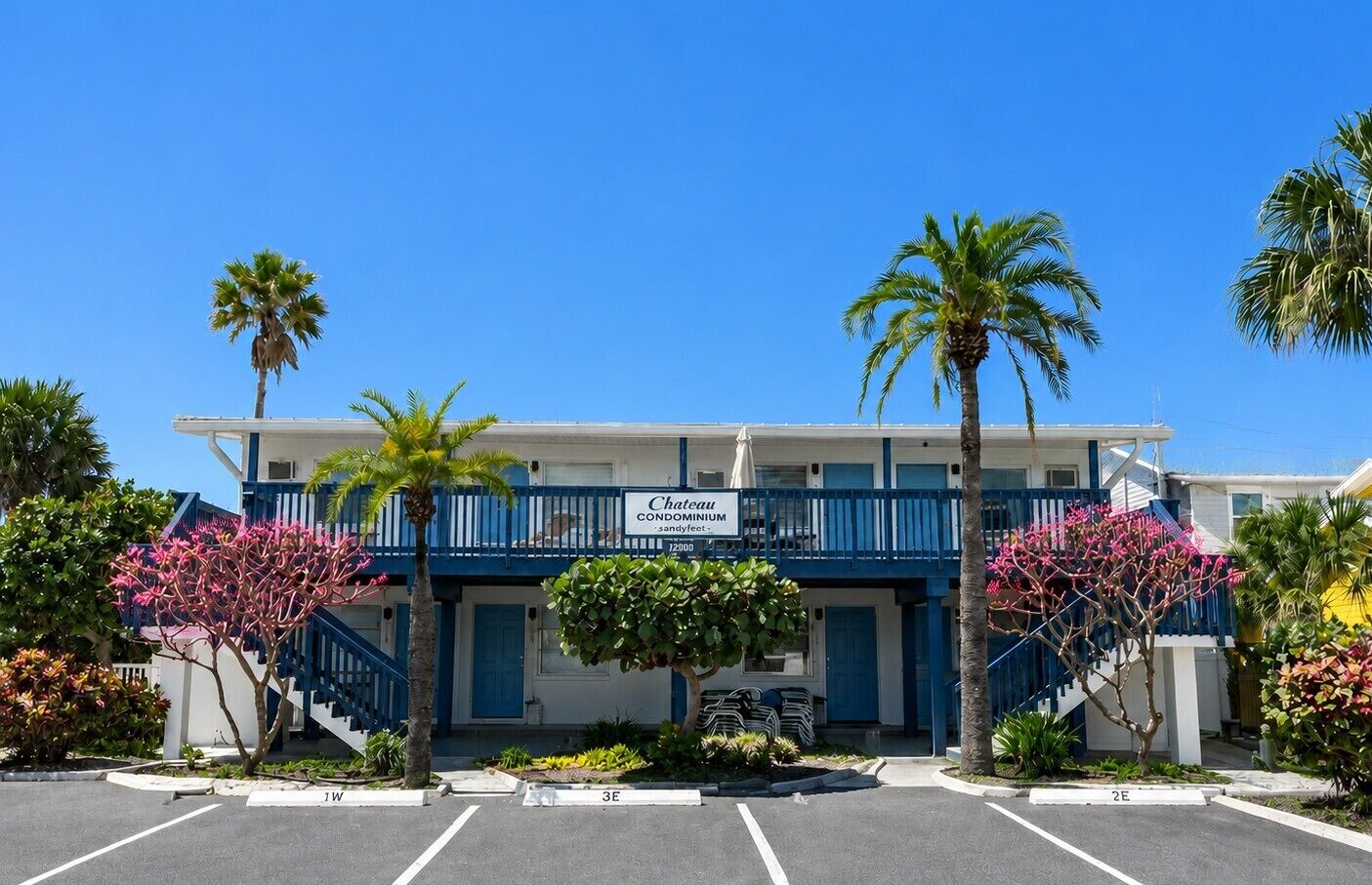Un hotel frente a la playa con fachada azul y blanca, un balcón y palmeras.
