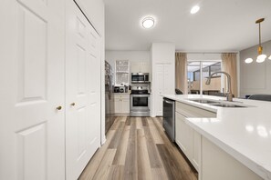 A modern kitchen with white cabinetry, stainless steel appliances, and a wooden floor. - 4720 HH - Fiesta Key Grandeur (Kissimmee)