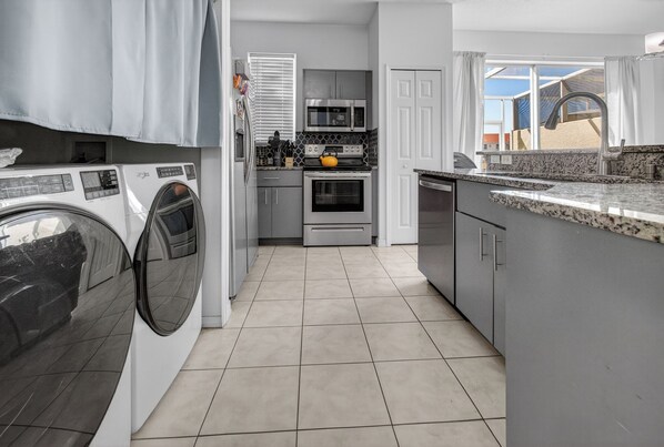A modern kitchen with a washing machine, microwave, oven, and granite countertop. - 4720 HH - Fiesta Key Grandeur (Kissimmee)