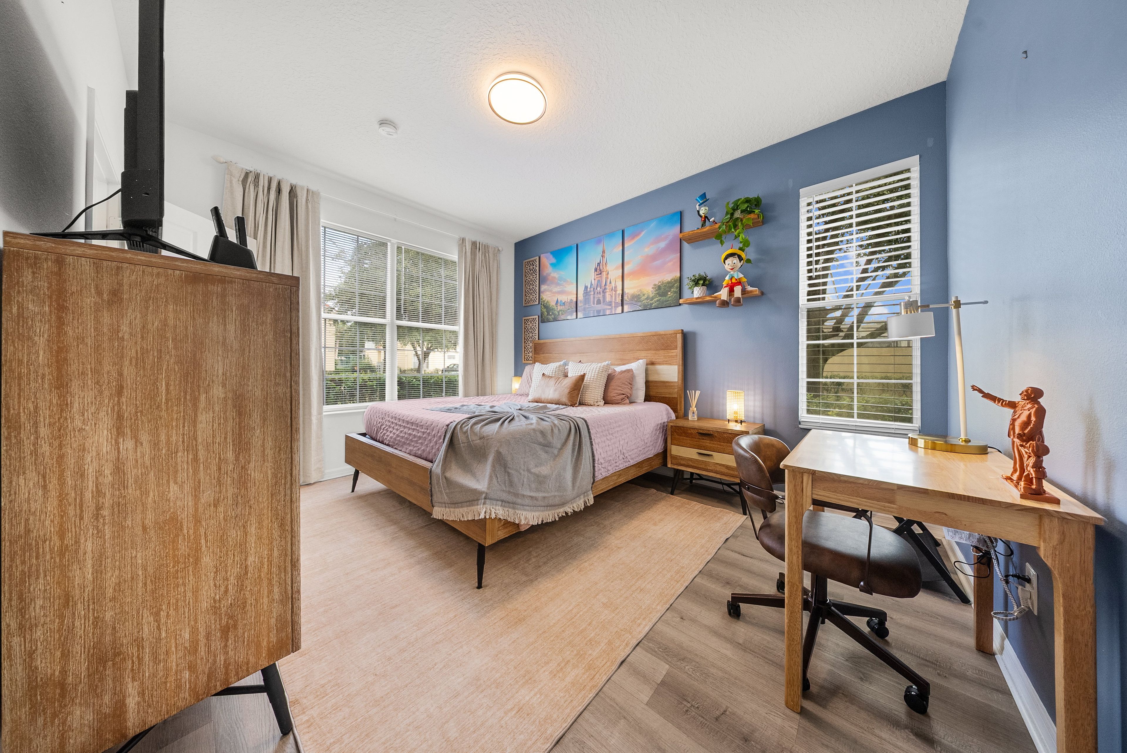 A bedroom with a bed, bedside table, desk, chair, and a window with blinds.