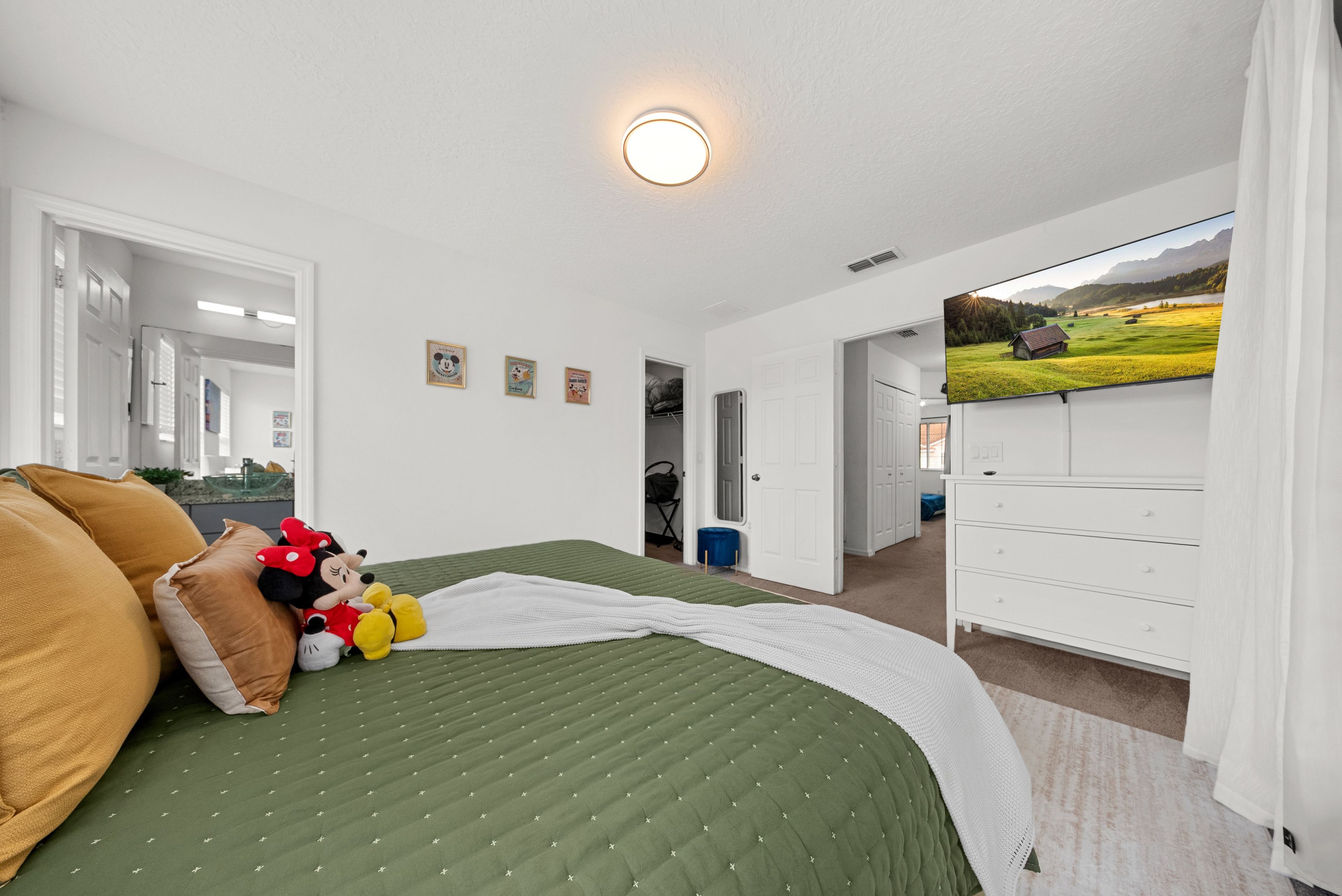 Un dormitorio con cama, almohadas, una colcha, televisor y cómoda.