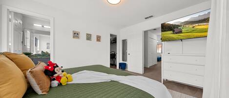 Un dormitorio con cama, almohadas, una colcha, televisor y cómoda.