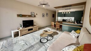 Een moderne woonkamer met een flatscreen televisie, een bank, een salontafel en een eethoek met stoelen.