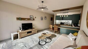 A modern living room with a flat-screen TV, a sofa, a coffee table, and a dining area with chairs.
