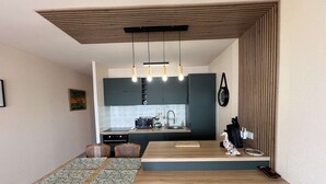 Een compacte keuken met donkere kastjes, een houten eettafel en een hangende lamp.