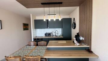 A compact kitchen with dark cabinets, a wooden dining table, and a hanging light fixture.
