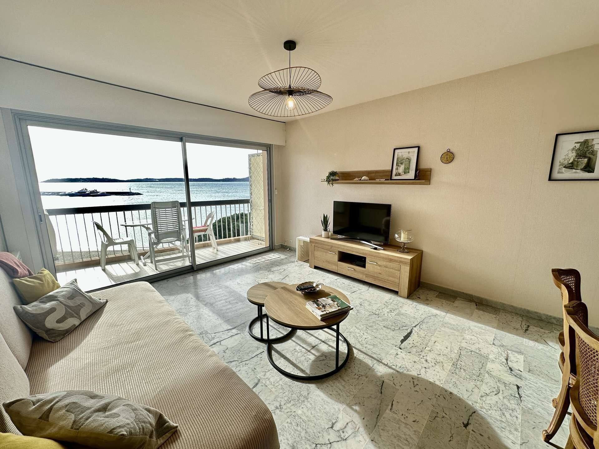 Un salon avec un canapé, une table basse, un téléviseur posé sur un meuble en bois et un balcon offrant une vue sur la mer.
