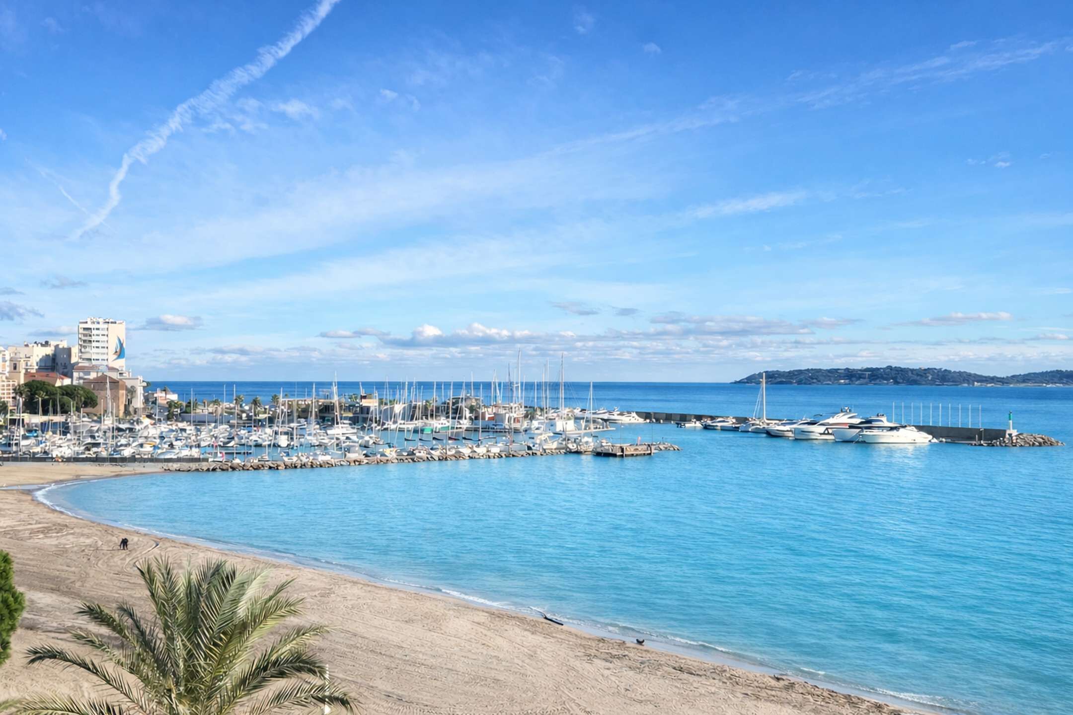 Un port de plaisance avec des bateaux amarrés, une plage de sable et un ciel bleu azur.
