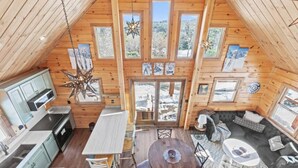 A wooden cabin with a kitchen, dining area, and living space, featuring large windows and a star-shaped light fixture. - North Star Trailside • Hiking • Moose Pond (Bridgton)