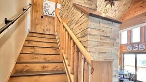 A wooden staircase with a handrail, leading to a room with a stone wall and a star-shaped light fixture. - North Star Trailside • Hiking • Moose Pond (Bridgton)