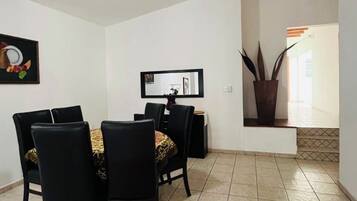 Un coin repas doté d’un ventilateur de plafond, d’une table à manger avec des chaises, d’un miroir et d’une plante en pot.