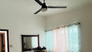 A bedroom with a bed, a desk with a mirror, a ceiling fan, and a window with curtains.