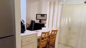 A compact kitchen with a refrigerator, a dining table with chairs, and a built-in oven.