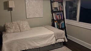 Un dormitorio con cama, estantería, ventana y lámpara en el techo.