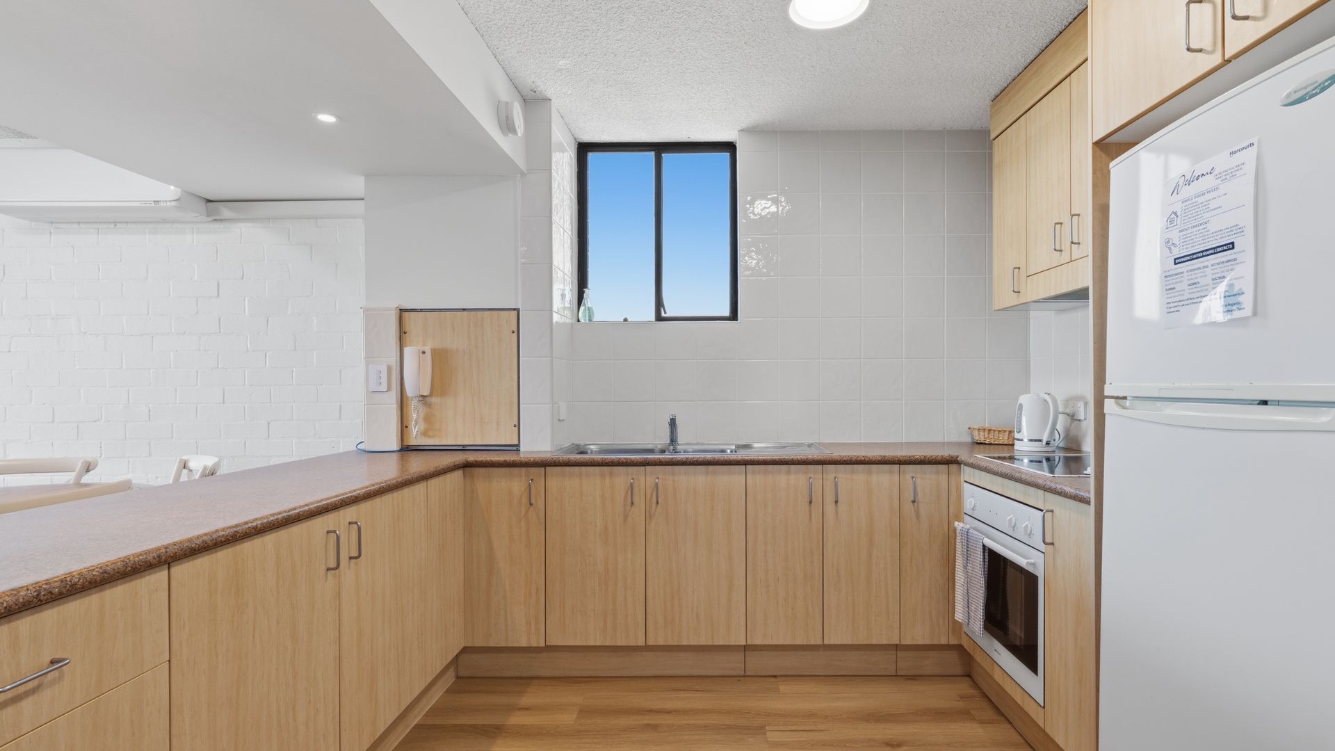 A modern kitchen with wooden cabinets, a built-in oven, and a window above the sink.