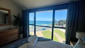Une chambre d’hôtel dotée d’une grande porte-fenêtre coulissante donnant sur un balcon avec vue sur l’océan et une route.