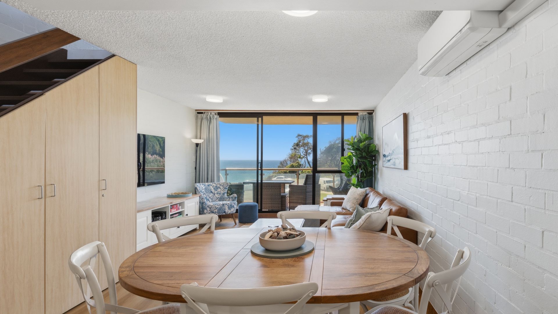 A dining area with a round table, chairs, and a view of the sea through large windows.