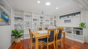 Un coin repas avec une table et des chaises en bois, entouré d’étagères blanches où sont exposés des tableaux encadrés.